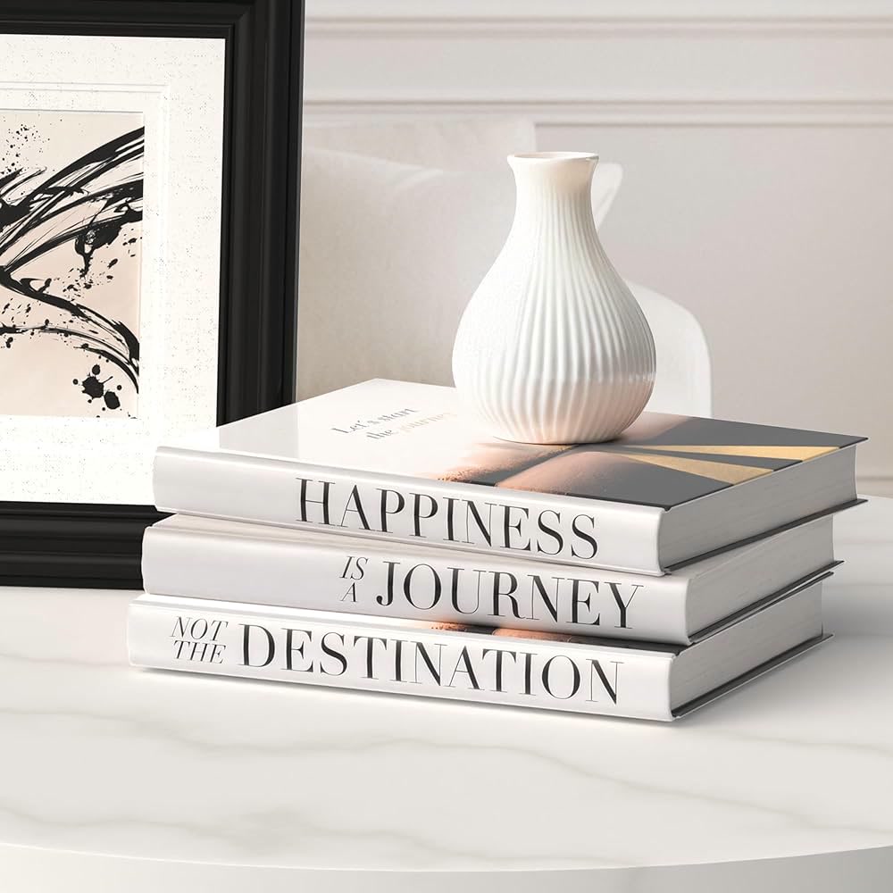 Trois livres blancs empilés sur une table, surmontés d'un vase
