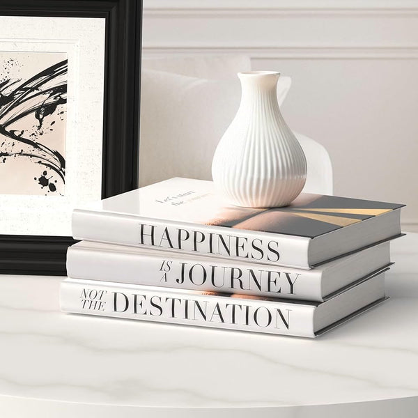 Trois livres blancs empilés sur une table, surmontés d'un vase